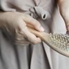 Close-up image of hands removing hair from a wooden brush, emphasizing daily hair care routine.
