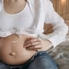 Close-up of a pregnant woman applying moisturizing lotion to her belly for skincare and maternity care.