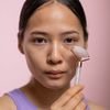 Close-up of a woman using a rose quartz facial roller in a studio setting.