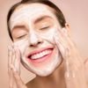 Smiling woman applies facial wash while enjoying her skincare routine, promoting happiness and skin health.